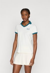 Λευκό πόλο με κοντά μανίκια και γιακά σε τυρκουάζ απόχρωση, με κεντημένο λογότυπο EA7 στο στήθος. Ομαλή υφή, ίσια κοπή και στρωματοποιημένος σχεδιασμός.