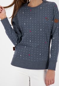 Szary sweter z białymi kropkami i małymi czerwonymi akcentami, wzory kotwic łodzi, ściągacze przy mankietach i dolnej części, z brązową skórzaną naszywką logo.