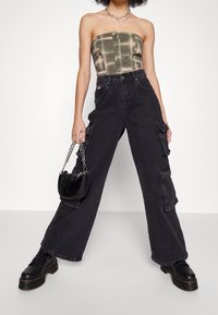 Svarta cargobyxor med vida ben, utrustade med flera fickor, bärs tillsammans med en grön rutig bhol top och svarta platåstövlar, samtidigt som en liten svart handväska hålls.