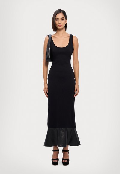 Robe noire à côtes avec un corsage ajusté et un ourlet en cuir évasé. Associée à des talons plates-formes noirs et un petit sac à bandoulière noir.