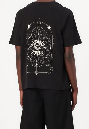 Sort T-shirt med et mystisk design med et centralt øje omgivet af stråler, stjerner, planeter og en halvmåne på ryggen.