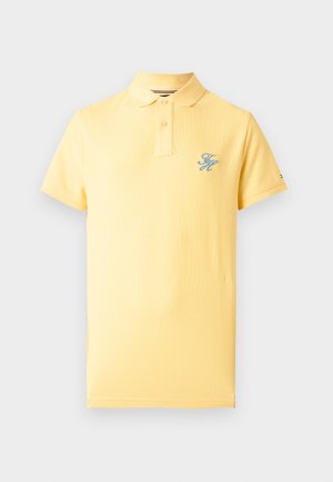 Κίτρινη πόλο μπλούζα με κοντά μανίκια, δύο κουμπιά και μικρό μπλε κεντημένο μονόγραμμα στο αριστερό μέρος του στήθους.