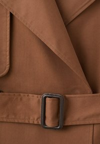 Hnedý trenčkot so širokými klopami a zodpovedajúcim látkovým opaskom s tmavou obdĺžnikovou prackou.