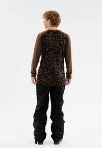 Langärmliges Shirt mit braunen Ärmeln und einem gemusterten schwarzen Körper, der großen, wiederholten Text zeigt. Kombiniert mit lockeren schwarzen Hosen.