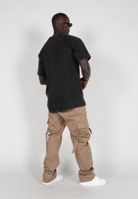 Camiseta de algodón negra de manga corta, combinada con pantalones cargo beige con bolsillos laterales y correas ajustables, llevada con zapatillas blancas.