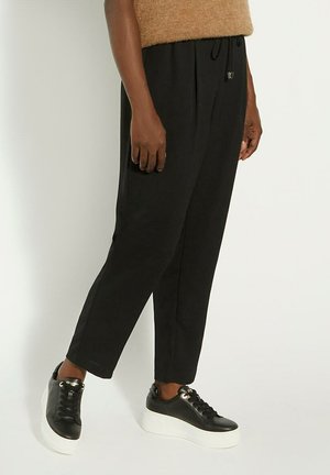 Pantalons noirs fuselés avec une taille à cordon de serrage, en tissu doux. Associés à des baskets noires avec une semelle plateforme blanche.