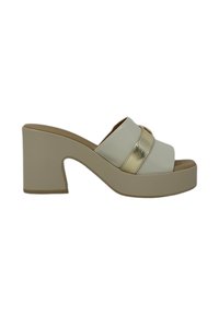 Scarpa piatta bianca da indossare senza lacci con un accento metallico dorato. Tacco spesso e design con punta aperta. Finitura liscia e leggero lucido sulla fascia.