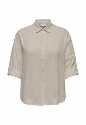 Chemise beige clair à boutons, manches retroussées et tissu texturé, avec un col classique et un ourlet droit.