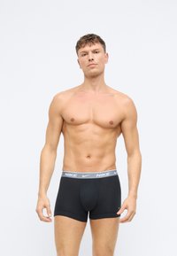 Fekete boxeralsó szürke gumiszalaggal, amelyen a Nike logó található. Az anyag lágy és szoros illeszkedésű, sima textúrával.