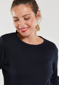 Maglione a coste blu navy con scollatura rotonda e una texture sottile. Dettagliato con maniche lunghe e abbinato a orecchini a forma di foglia d'oro.