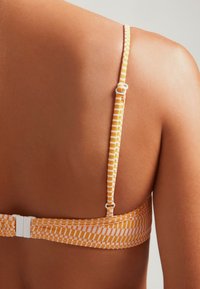 Top de bikini a rayas naranjas y blancas con un diseño texturizado, que cuenta con tirantes ajustables y un cierre de hebilla en la parte posterior.