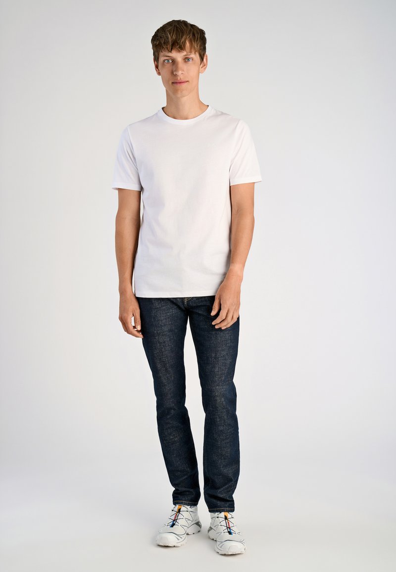 Biała koszulka z krótkim rękawem, ciemnoniebieskie dżinsy i białe trampki z wielokolorowymi akcentami. Prosty design, luźny krój, gładka tekstura.