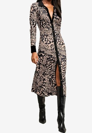 Femme portant une robe longue à manches longues à imprimé léopard avec bordure noire et des bottes noires montant jusqu'aux genoux, debout avec une jambe légèrement en avant.