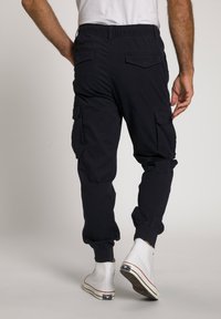 Navy cargobroek met elastische manchetten, twee zijzakken en een tailleband met trekkoord; gecombineerd met witte hoge sneakers.