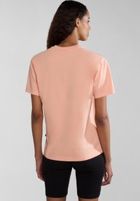 Kurzärmliges, pfirsichfarbenes Baumwoll-T-Shirt mit lockerer Passform, rundem Halsausschnitt und einem abgerundeten Saum, kombiniert mit schwarzen Shorts.