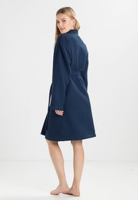 Peignoir de bain en bleu marine avec une texture en gaufre, des manches longues, une taille ceinturée et une coupe à mi-cuisse. Tissu doux au design classique.