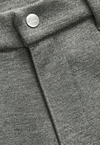 Grå texturerad tyg med en närbild av en platt framsida och en silverfärgad knappknäppning, med släta sömdetaljer.