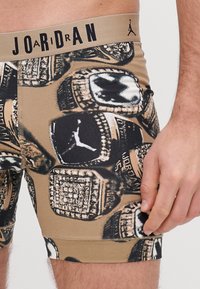 Férfi boxernadrág világosbarna színben, ismétlődő fekete-fehér grafikával, amely bajnoki gyűrűket ábrázol. Rugalmas derékpánt "JORDAN" logóval.