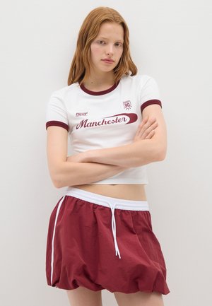 Witte cropped t-shirt met bordeaux accenten en de tekst "Manchester", gecombineerd met losse bordeaux shorts met een witte trekkoord en zijstroken.
