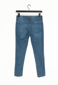 Pantalones vaqueros de denim azul con un corteSlim, que presentan un dobladillo deshilachado y dos bolsillos traseros. El material tiene una textura suave con ligeros detalles de desgaste.