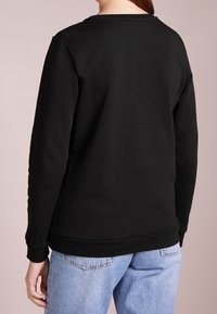 Sudadera negra con cuello redondo, puños acanalados y dobladillo recto. Tela suave. Llevada con jeans de corte holgado en azul claro.