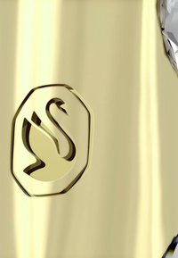 Superficie dorada con un logotipo de cisne en relieve dentro de un contorno hexagonal y una textura brillante y reflectante.