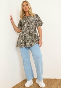 Beige peplum top met luipaardprint en korte mouwen, gecombineerd met lichtblauwe rechte jeans en witte platform sneakers. Gestructureerde stof.