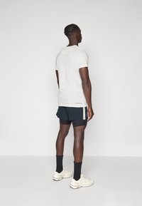 Vit kortärmad t-shirt kombinerad med svarta shorts med sidodetaljer. Modellen bär vita sneakers och svarta strumpor.