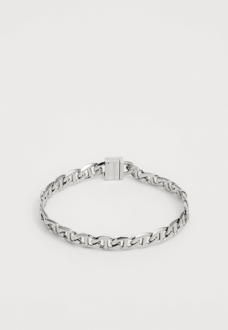 Bracelet en chaîne argentée avec fermoir rectangulaire gravé du nom de la marque, posé à plat sur un fond blanc uni.