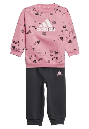Felpa rosa con motivi grafici neri e logo Adidas bianco, abbinata a pantaloni della tuta grigio scuro con logo rosa. Materiale in cotone morbido.