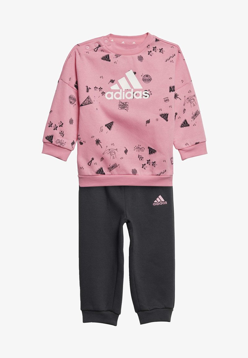 Felpa rosa con motivi grafici neri e logo Adidas bianco, abbinata a pantaloni della tuta grigio scuro con logo rosa. Materiale in cotone morbido.