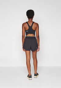 Sostén deportivo negro con diseño de espalda nadadora, combinado con pantalones cortos deportivos negros que cuentan con una cinturilla contrastante y acentos de logotipo.