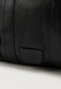 Melnas ādas soma ar teksturētu virsmu, kas dekorēta ar vertikālām svītrām un mazu taisnstūra birku. Matēta apdare un tīrs dizains.