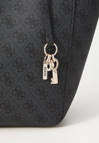 Borsa nera a trama testurizzata con motivo in rilievo, dotata di hardware dorato, un portachiavi con chiave e un'etichetta con la scritta "GUESS."