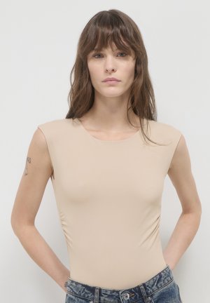 Body nudo con maniche a cappuccio, texture liscia e scollatura rotonda, abbinato a jeans di denim strappati a vita alta.