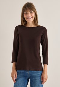 Braunes Langarmoberteil mit Boots-Ausschnitt und lässigem Schnitt, kombiniert mit blauen Jeans. Glatte Textur, einfaches Design und keine Verzierungen.