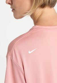 Camiseta atlética transpirable de color rosa con un tejido texturizado, que presenta un logo de Nike blanco en el hombro y un cuello redondo.
