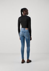 Black long-sleeve top paired with blue skinny jeans featuring a distressed knee, metal hardware, and a branded leather patch at the waist.