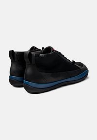 Zapatillas negras con parte superior de cuero suave, punta redonda y suela de goma azul contrastante. Presentan cordones y detalles de costura mínimos.
