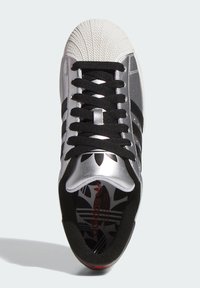 Baskets argentées avec embout en caoutchouc, lacets noirs et trois bandes noires. Semelle intérieure à motif noir et blanc.