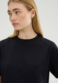 Czarna bawełniana koszulka z okrągłym, ribbed dekoltem, krótkimi rękawami i dyskretnym wytłoczonym logo. Gładka tekstura i luźny krój.