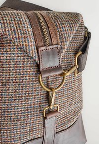 Messenger bag featuring a textured brown fabric with multicolored flecks, brown leather accents, a gold zipper, and metal hardware.