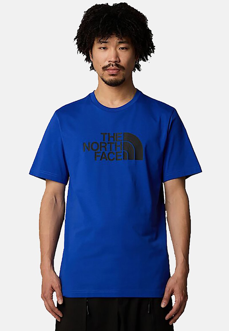 Camiseta de cuello redondo azul, hecha de una mezcla de algodón, con un logo impreso en negro de "The North Face" en el frente. Mangas cortas con un ajuste relajado.