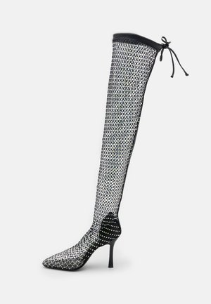 Stivale in rete nera al ginocchio con tacco a spillo e punta affusolata, caratterizzato da un motivo di strass e un bordo superiore nero con dettaglio lacciato.