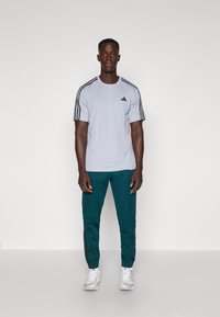 Lichtgrijs sportshirt met korte mouwen, voorzien van zwarte strepen en logo, gecombineerd met donkerblauwe joggers met zijstrepen en elastische boorden.