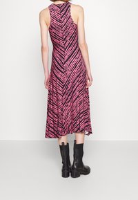 Różowa i czarna sukienka w paski zebry bez rękawów z rozkloszowanym fasonem, sięgająca do połowy łydki, zestawiona z czarnymi botkami za kostkę.