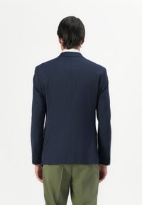 Navyblazer med en skreddersydd passform, enkelt hull og to knappelukking, kombinert med lysegrønne bukser. Glatt tekstur og strukturert design.