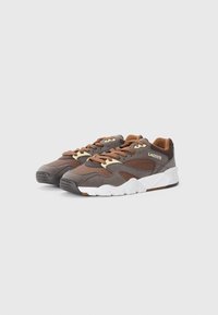 Brown suede and textile sneakers with white rubber sole, featuring brown laces and subtle perforations. Lacoste logo on the side.