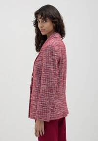 Blazer rosso strutturato con un motivo intrecciato, colletto a revers e chiusura con un solo bottone, abbinato a pantaloni rossi coordinati.