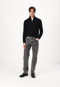 Crna zip-up dukserica, sivi traperice s izblijedjelim završetkom, crne kožne čizme, stoji na bijeloj pozadini. Minimalni detalji.